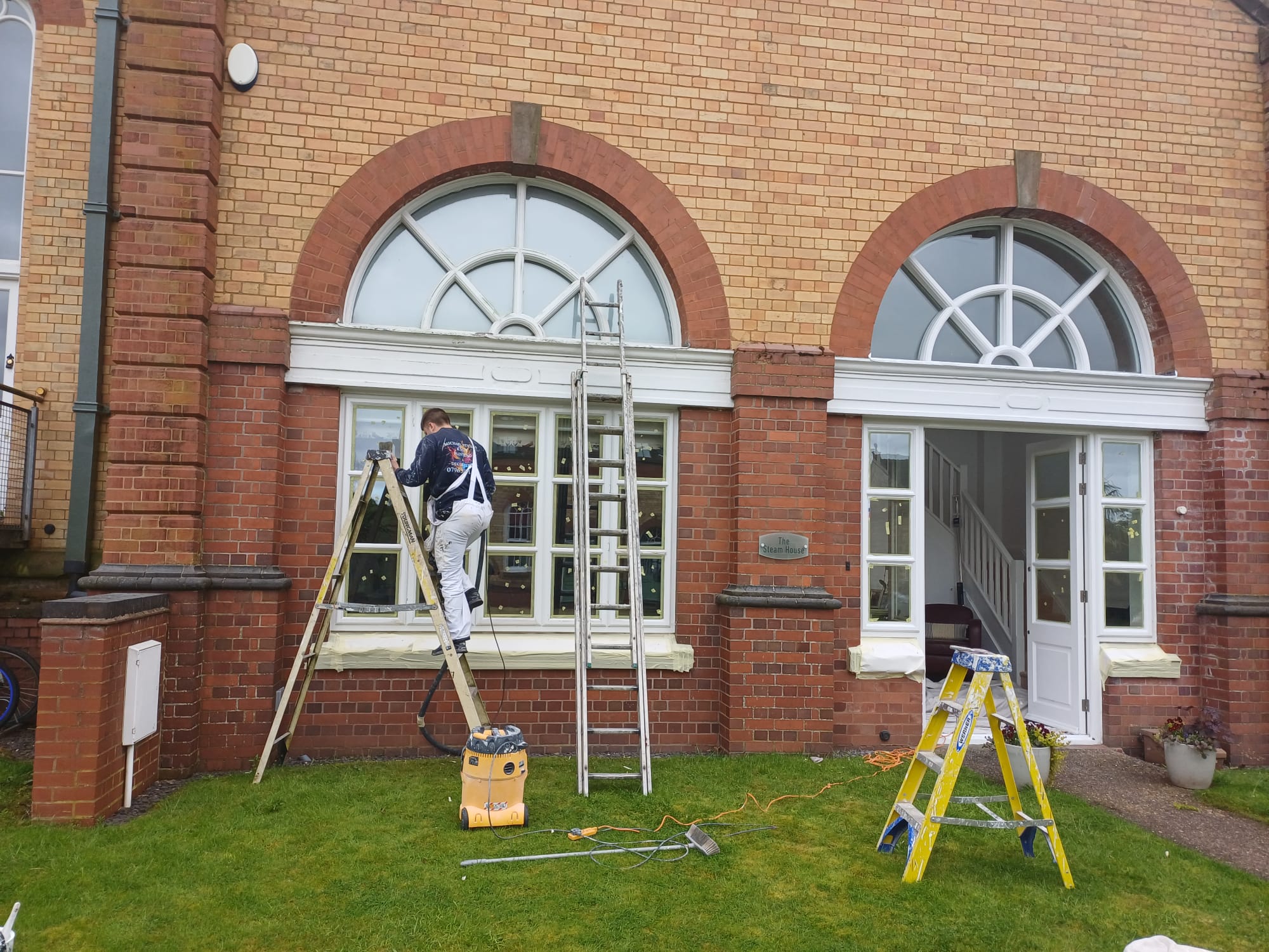 Decorator on a ladder painting exterior window frames of a brick building